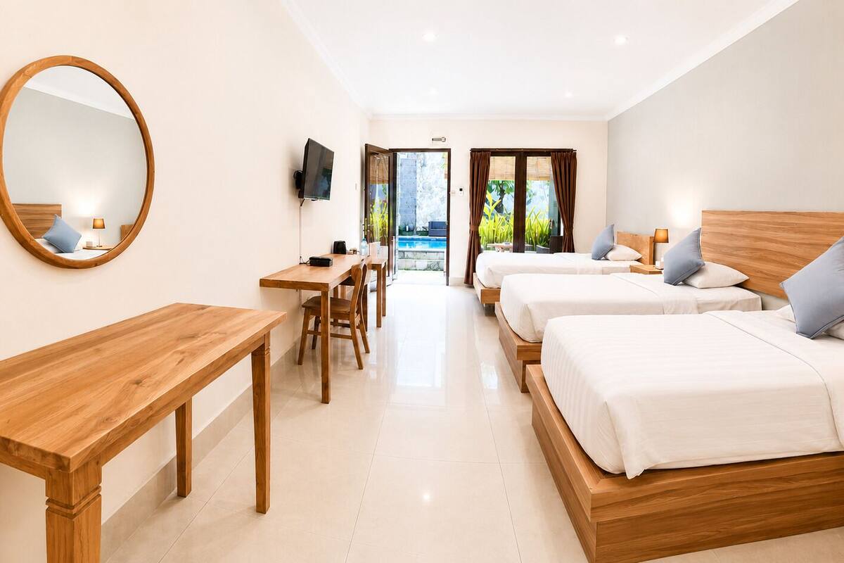Une chambre d’hôtel avec trois lits, un bureau en bois, une télévision et une vue sur l’extérieur.