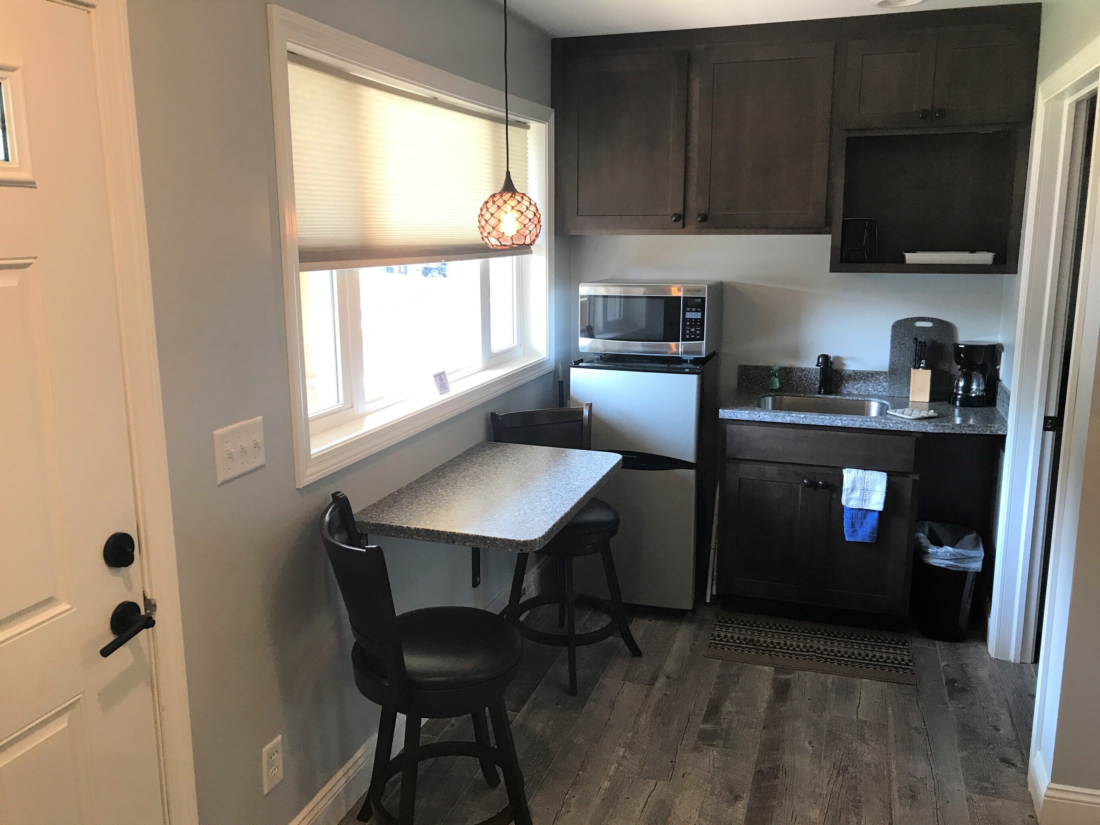 Cocina compacta con microondas, pileta y pequeño comedor para dos personas.