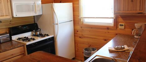 A compact kitchen with wooden cabinets, a microwave, a stove, a refrigerator, and a sink.