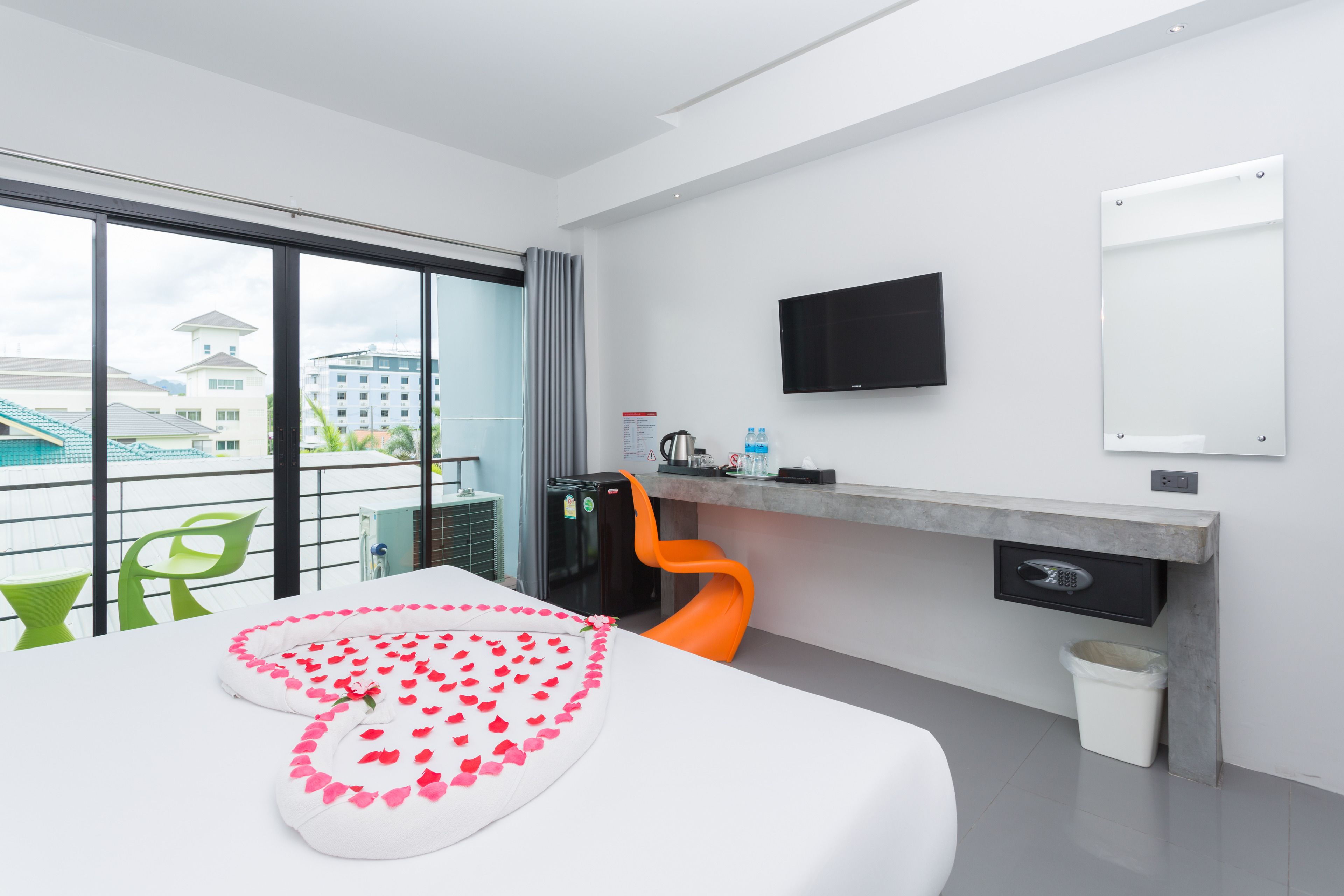 Una habitación de hotel moderna con un gran ventanal, un televisor de pantalla plana, un escritorio con una silla y una cama decorada con pétalos de rosa.