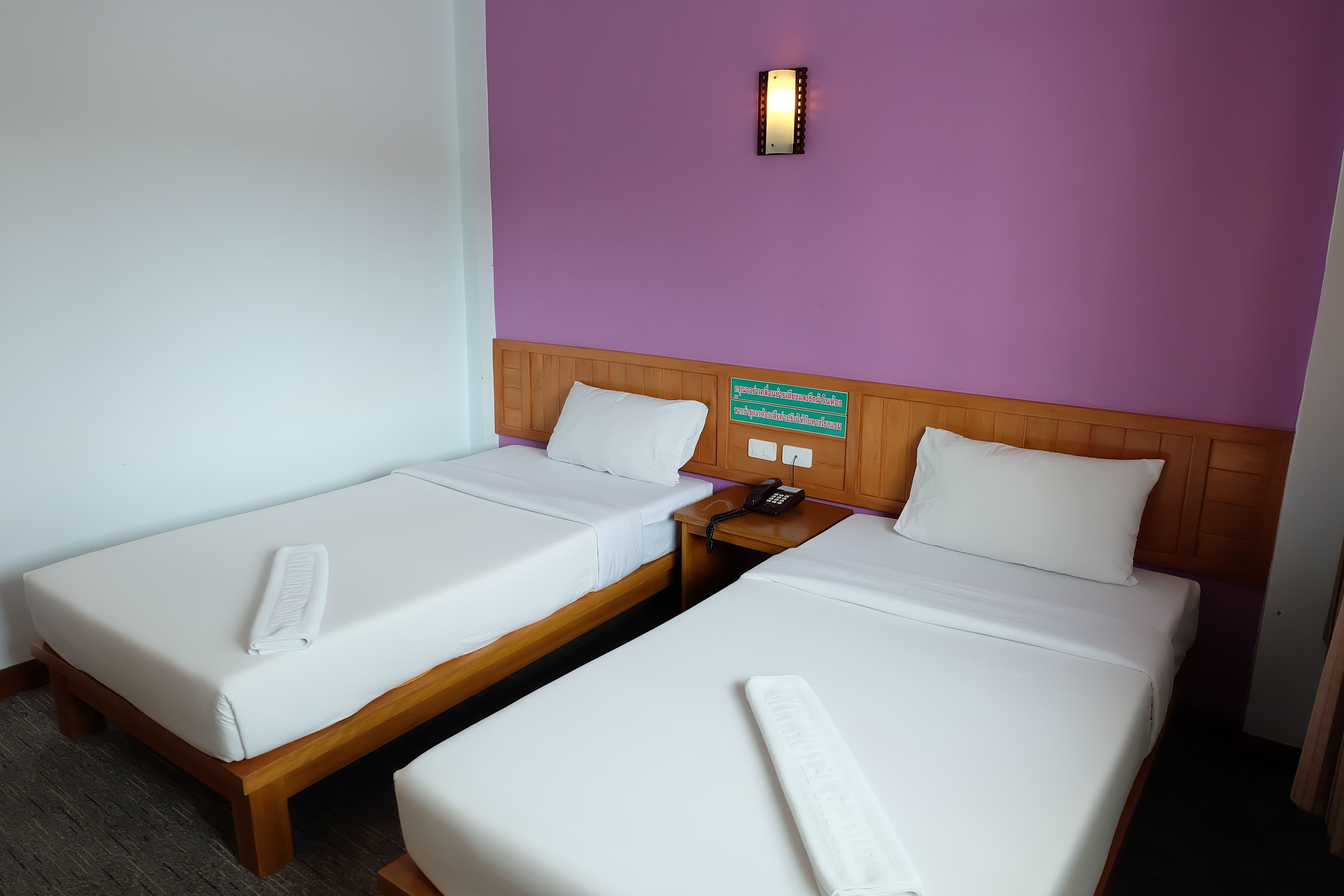 Habitación de hotel con dos camas individuales, cabecera de madera, mesita de noche con teléfono y un cartel con el número de la habitación.