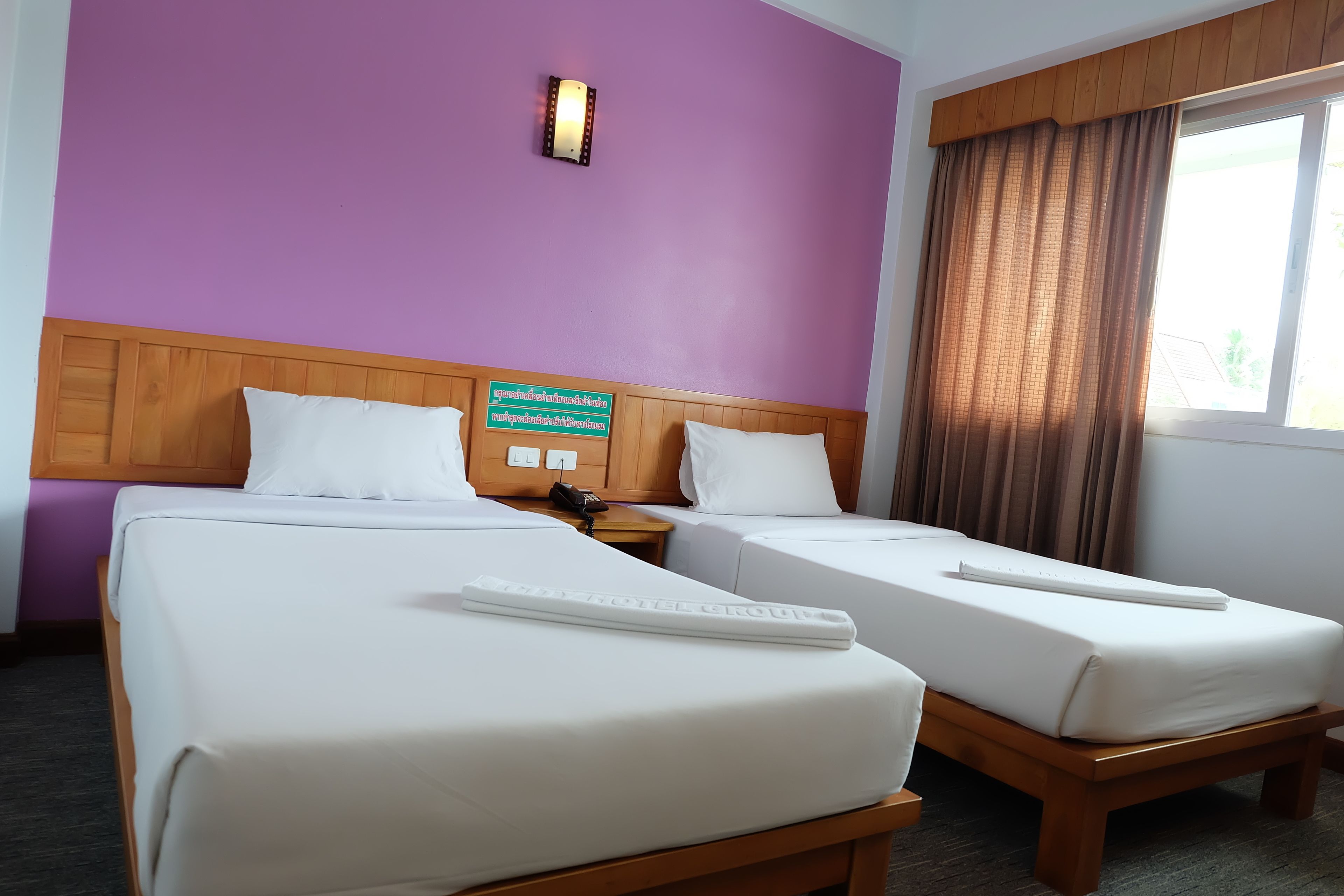 Habitación de hotel con dos camas, cabecero de madera, un cartel en la pared y una ventana con cortinas.