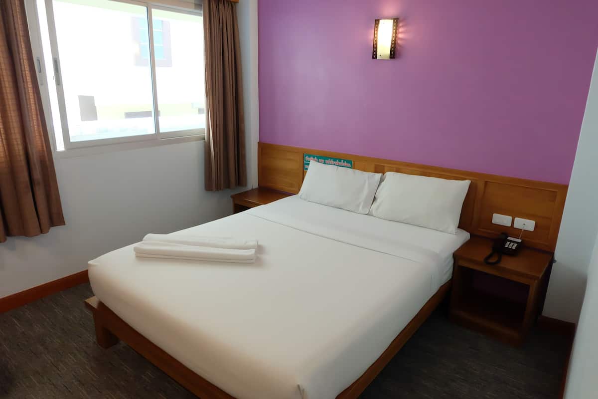 A neatly made bed with white linens, a wooden headboard, and a nightstand with a phone.