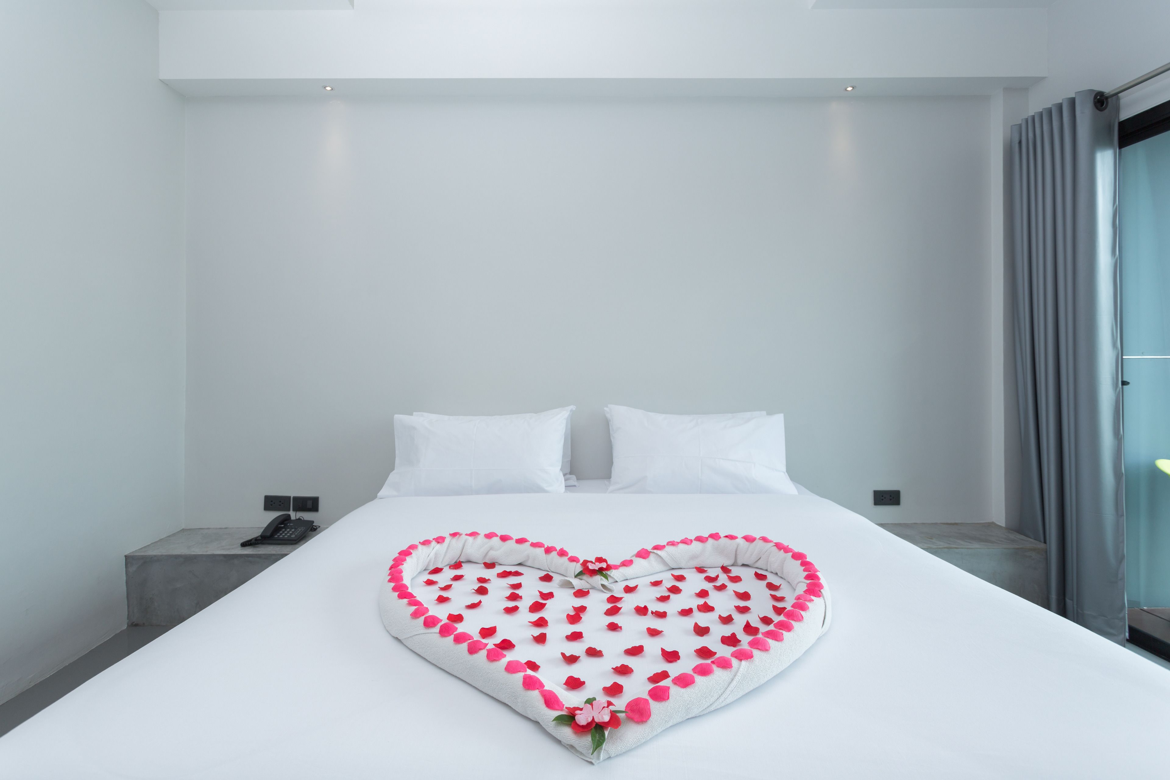 A modern hotel room with a neatly made bed, a bedside phone, and a view of the city through the window.