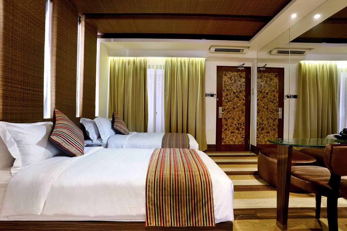 Een hotelkamer met twee bedden, een glazen tafel en een bruine leren stoel.