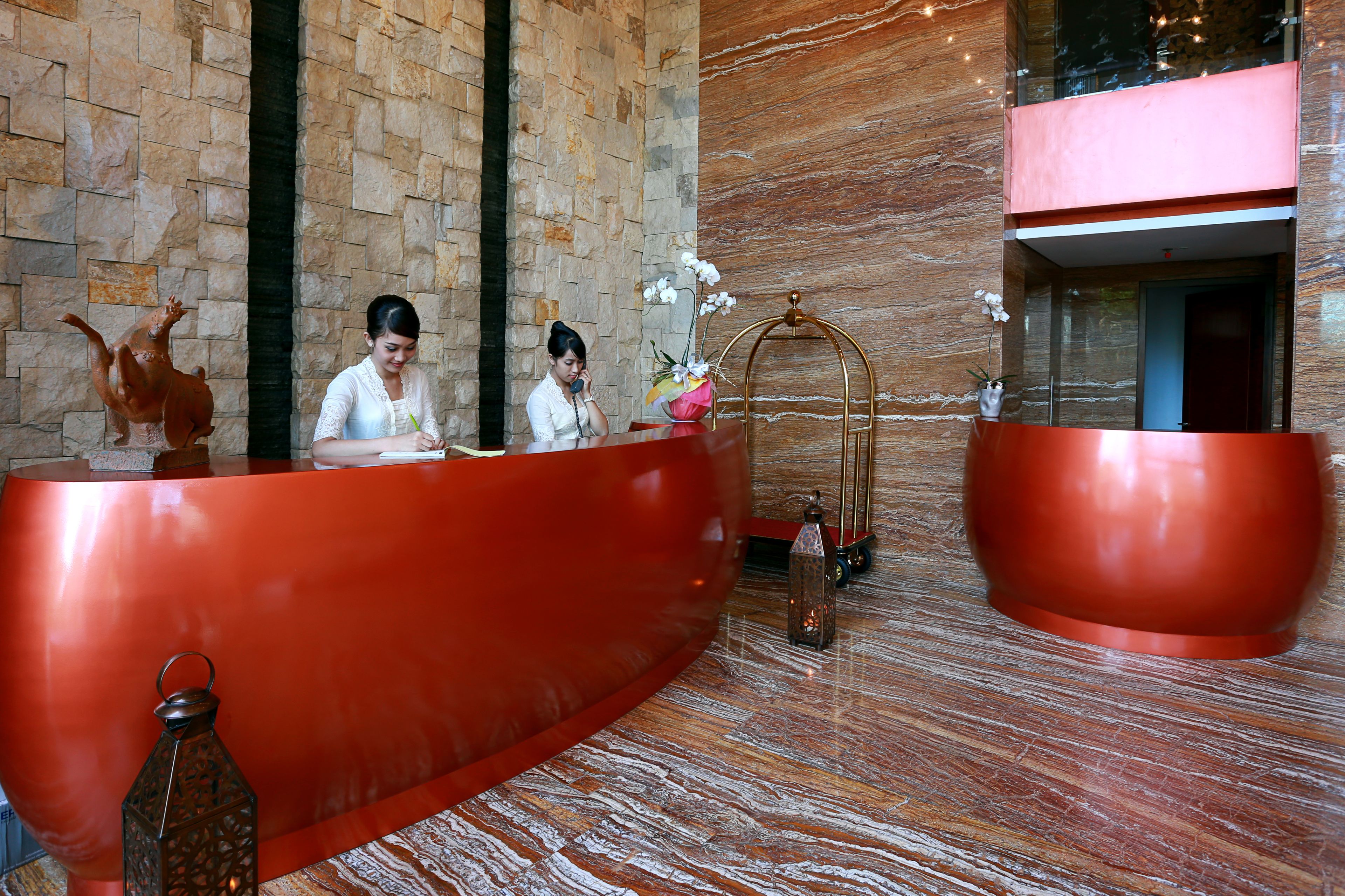 A reception area with a large red reception desk, a stone wall, and a marble floor.