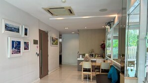 A modern living room with a sofa, a dining table, and chairs. There are framed pictures on the wall and a window with a view of greenery. - S3 Residence Park (Bangkok)