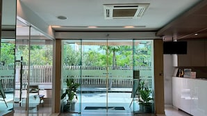 A modern hotel lobby with a glass door leading to a balcony, potted plants, and a flat-screen TV on the wall. - S3 Residence Park (Bangkok)