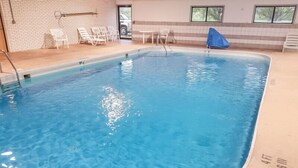 Una piscina interior con agua azul cristalina, rodeada de sillas de descanso y una pared de azulejos.