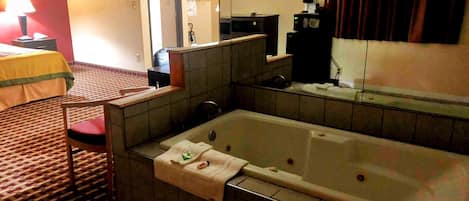 Una habitación de hotel con una bañera grande, un escritorio con lámpara, un televisor y un espejo.