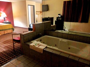 A hotel room with a large bathtub, a desk with a lamp, a television, and a mirror.