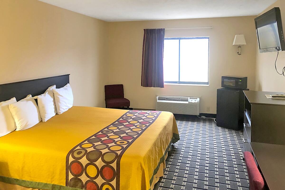Habitación de hotel con una cama grande, un escritorio, una silla, un televisor y una ventana con cortinas.