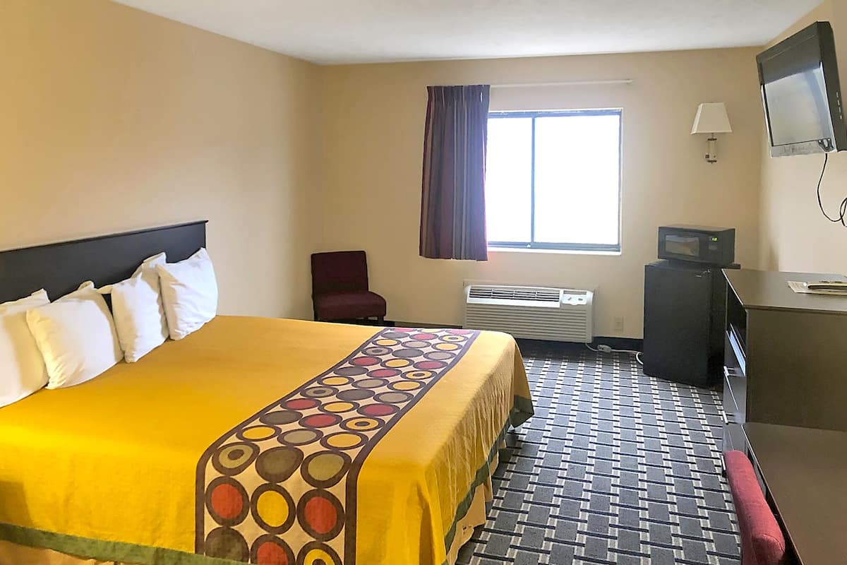 A hotel room with a large bed, a desk, a chair, a television, and a window with curtains.
