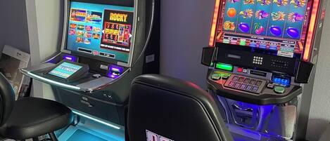 Two slot machines with a J&J Gaming logo, a television above the left machine, and a chair in front.