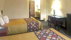 Una habitación de hotel con dos camas, un escritorio, una silla, un espejo y una lámpara.