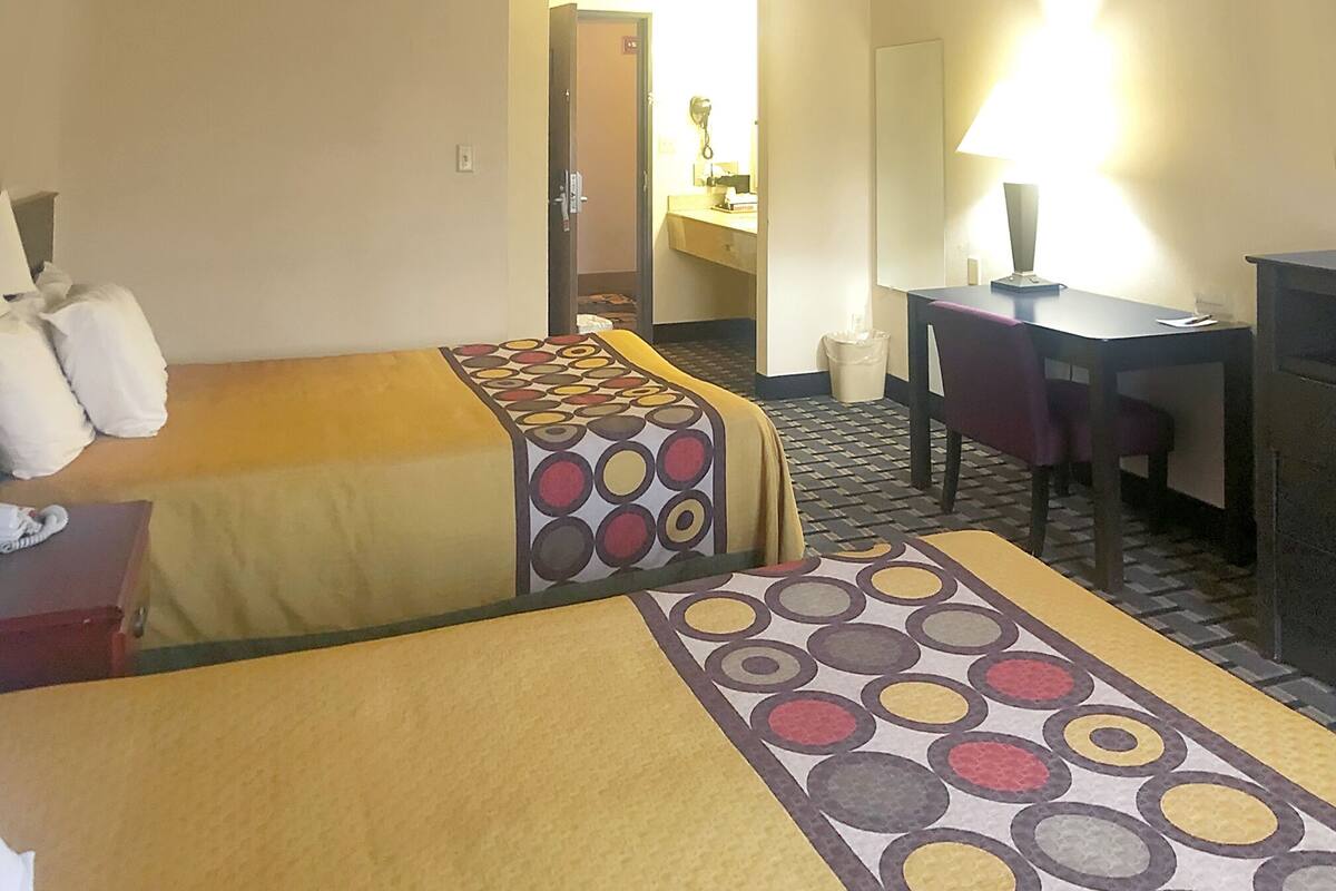 Una habitación de hotel con dos camas, un escritorio, una silla, un espejo y una lámpara.