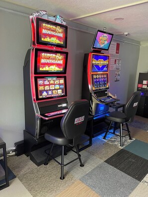 Two gaming machines with illuminated screens, a selection of chairs, and a wall-mounted sign. - Hotel 7 Vienna (Vienna)