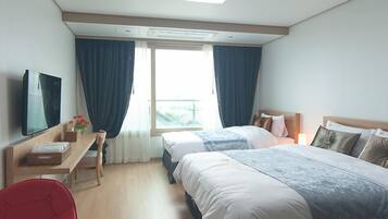 A hotel room with two beds, a desk with a chair, a TV, and a balcony with curtains.