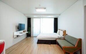 A modern hotel room with a bed, a green sofa, a TV, and a window with curtains.