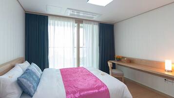 A hotel room with a bed, a desk, and a window with curtains.