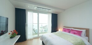 A hotel room with a bed, a TV, a window with curtains, and a balcony with outdoor furniture.