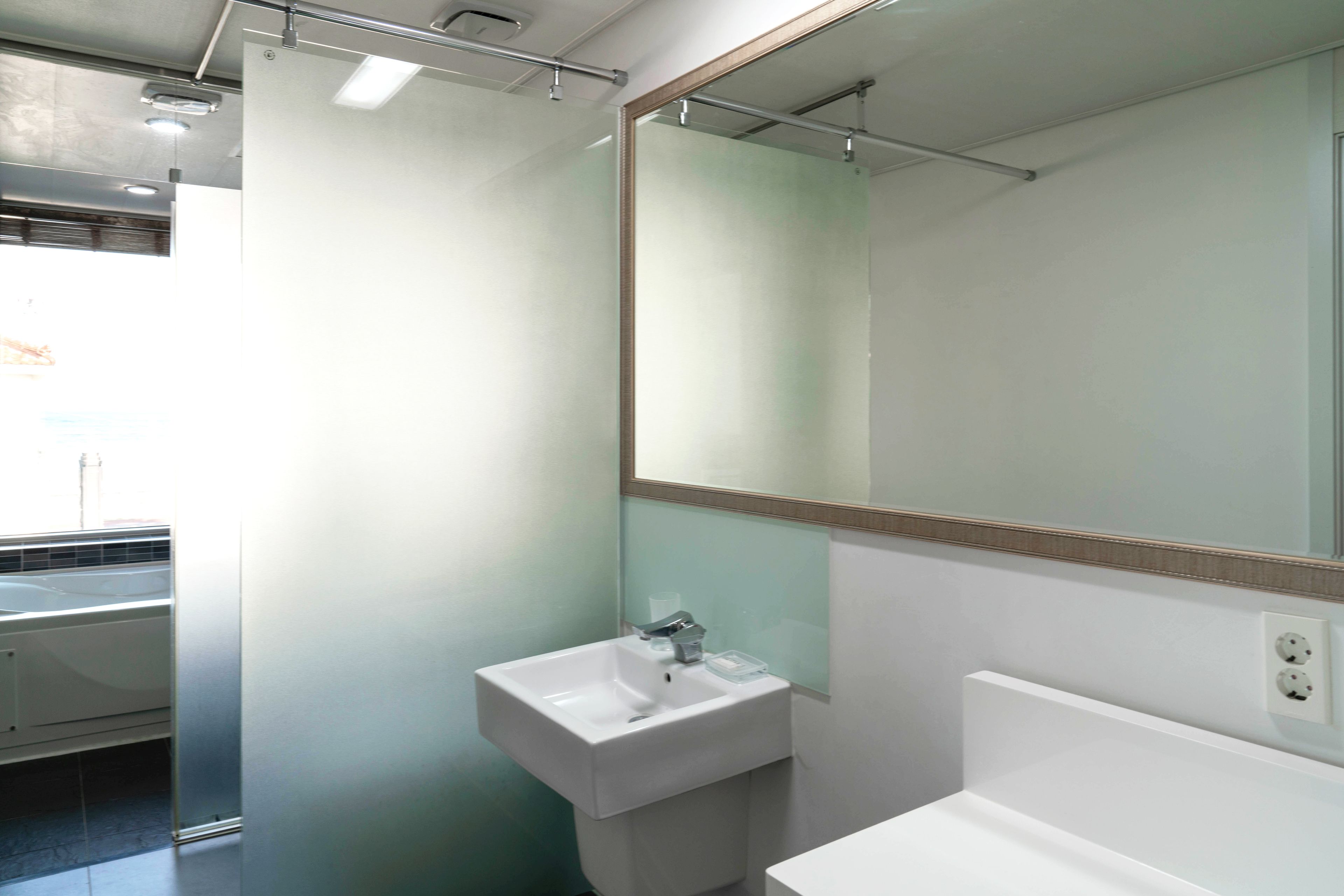 A bathroom with a white sink, a mirror, and a window.