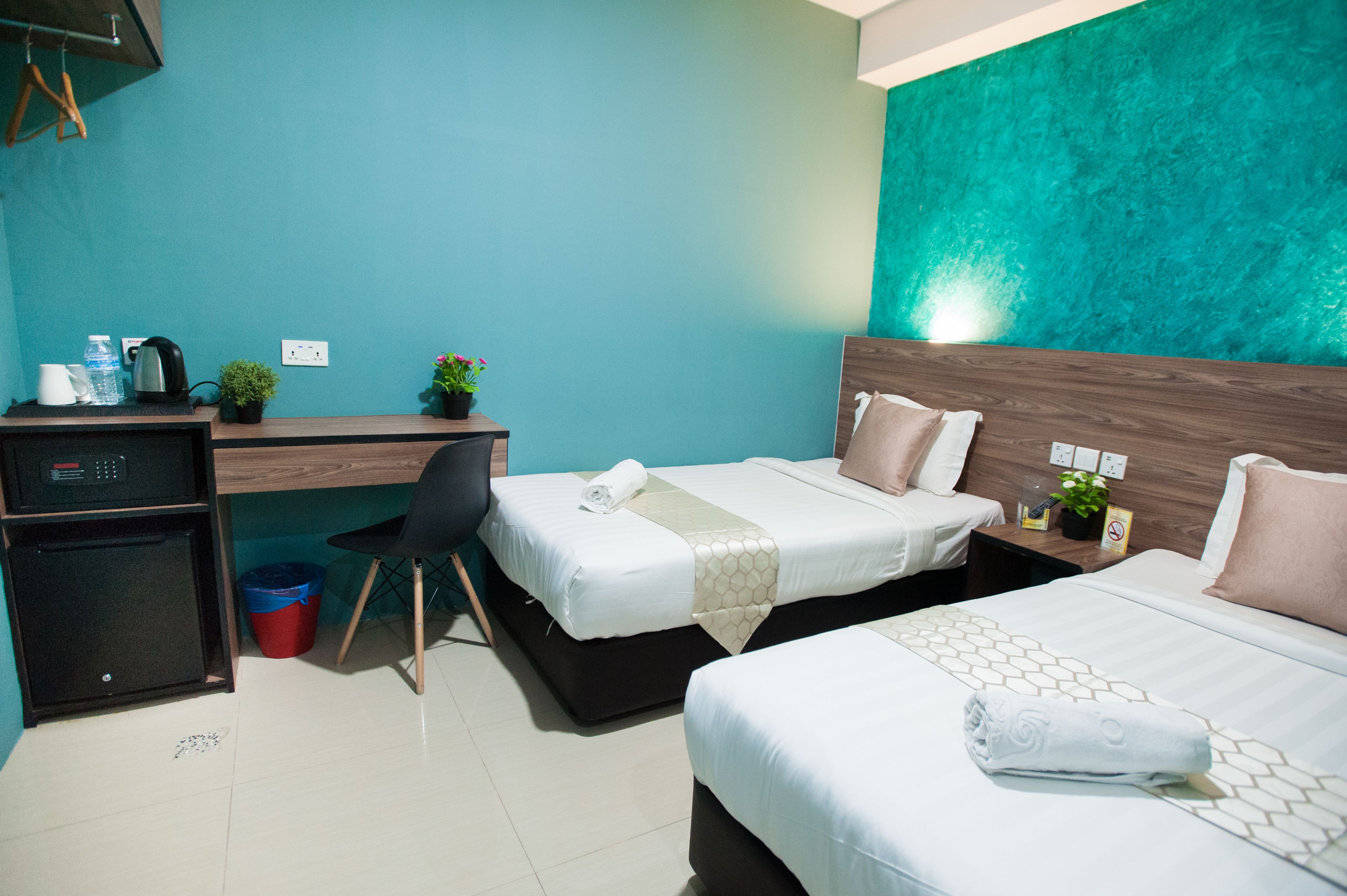 A hotel room with two beds, a desk, a chair, a small fridge, and a trash bin.