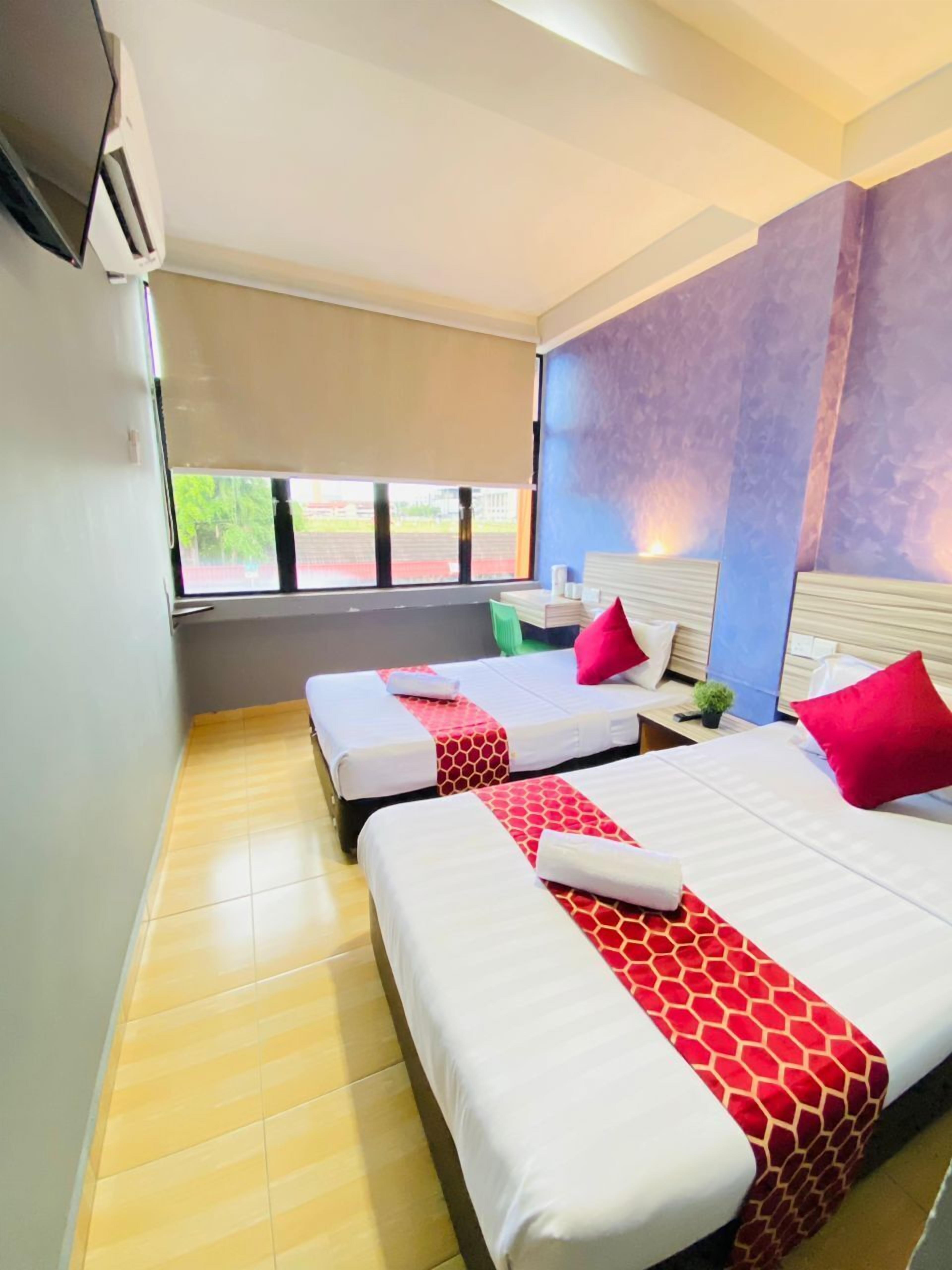 A hotel room with two beds, a window with a view, and a wall-mounted air conditioner.