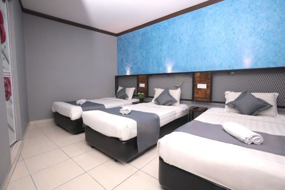 Une chambre d’hôtel avec trois lits, un grand mur bleu à texture et un sol carrelé.