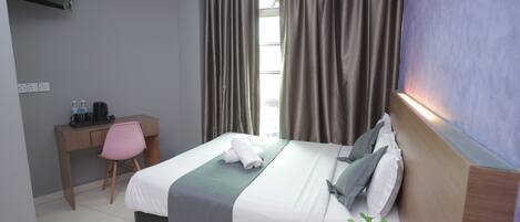 A hotel room with a bed, a desk, a chair, a TV, and a window with curtains.
