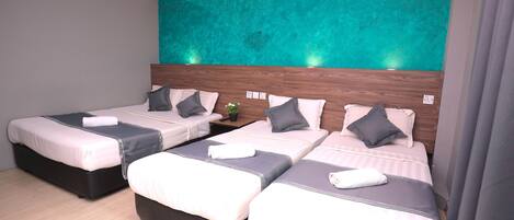 Quarto de hotel com três camas, cada uma com cabeceira de madeira, roupa de cama cinza e branca, e uma parede de destaque azul-esverdeado.