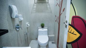 Une petite salle de bain comprenant des toilettes, un distributeur de savon liquide, un distributeur d’essuie-tout et une petite plante en pot.