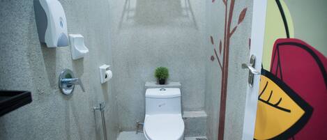 A small bathroom with a toilet, a hand soap dispenser, a paper towel dispenser, and a small potted plant.