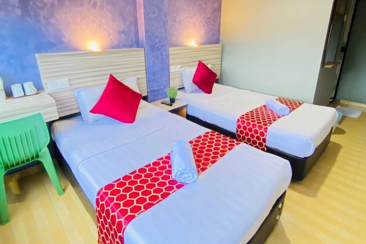 A hotel room with two beds, each with a headboard, a green chair, and a nightstand with a lamp.