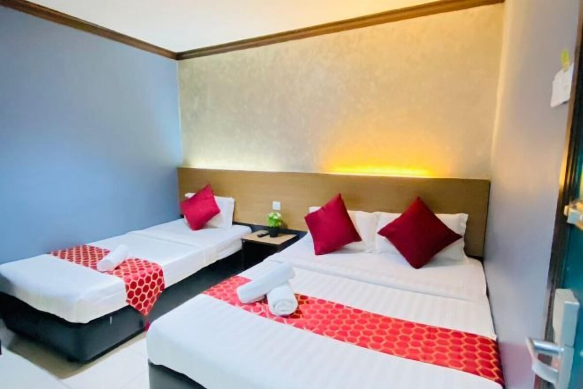 Une chambre d’hôtel avec deux lits, chacun agrémenté de draps blancs et de touches de couleur rouge, une table de chevet avec une lampe et une tête de lit dotée d’un luminaire.