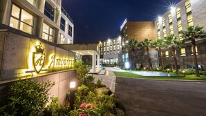 Una entrada de hotel con un cartel bien iluminado, un jardín ajardinado y una fachada de edificio moderna.