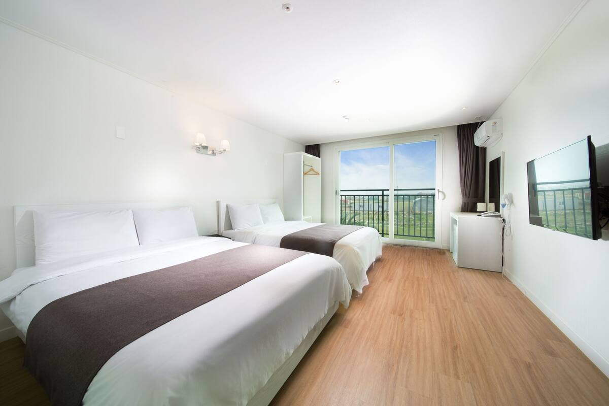 Hotellihuone, jossa on kaksi sänkyä, televisio, parveke ja pieni työpöytä.