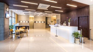 Un  área de recepción moderna con un mostrador blanco, paneles de madera y plantas en macetas.
