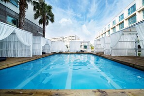 A swimming pool with white canopies and wooden deck, surrounded by modern buildings. - Amoureux (Jeju City)