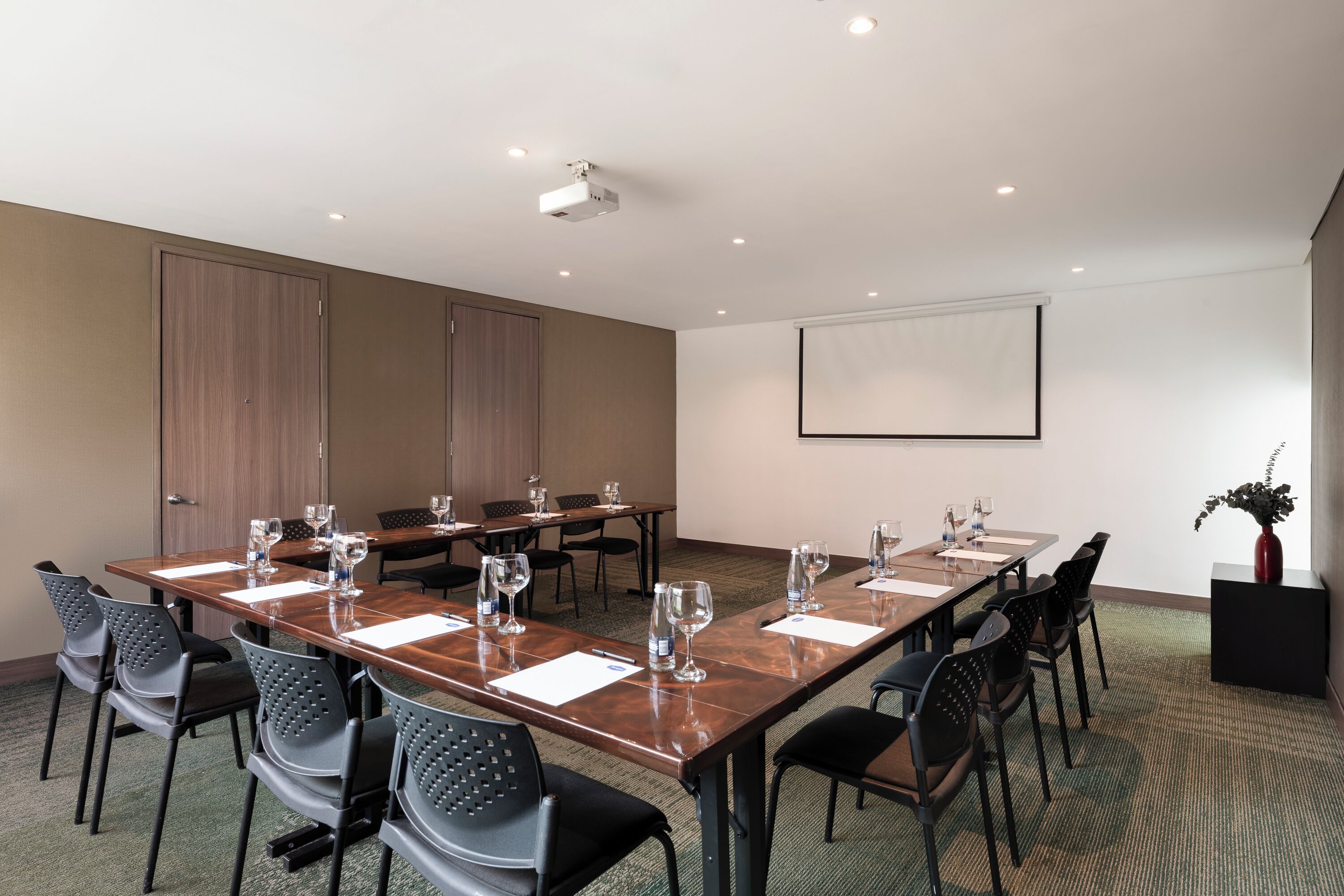A conference room with a long table, chairs, a projector, and a screen.