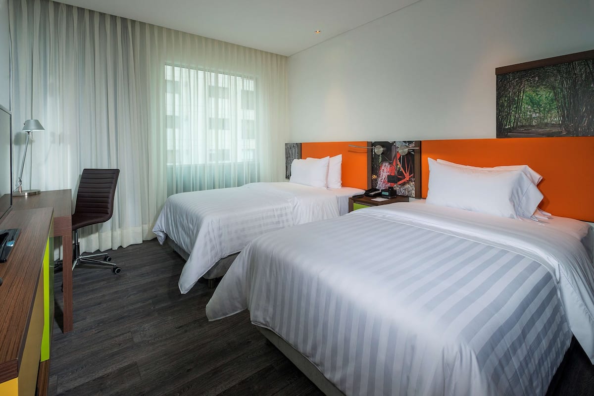 A hotel room with two beds, a desk, a chair, and a large window with curtains.