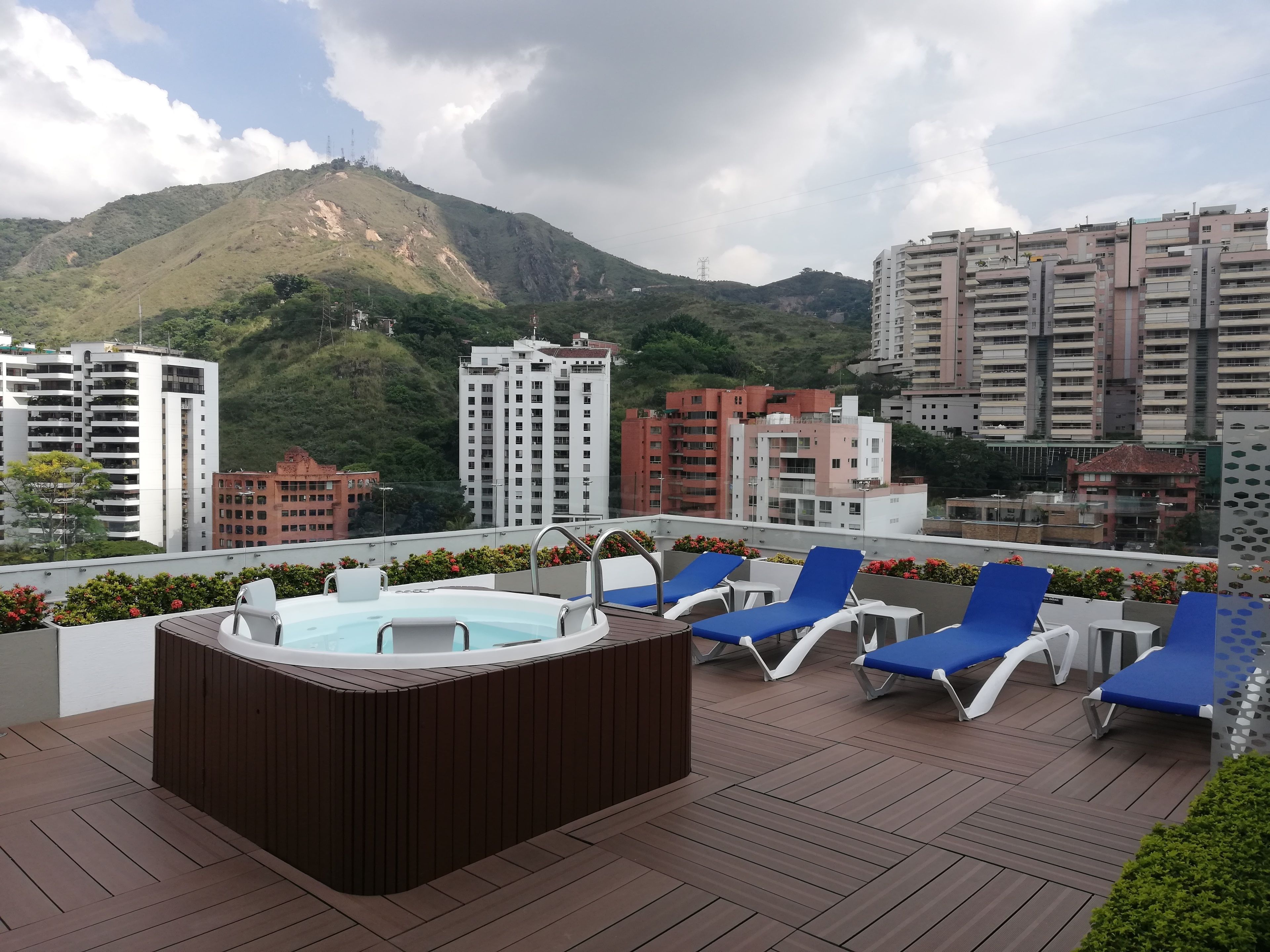 A rooftop terrace with a hot tub, lounge chairs, and a view of a mountain and buildings.