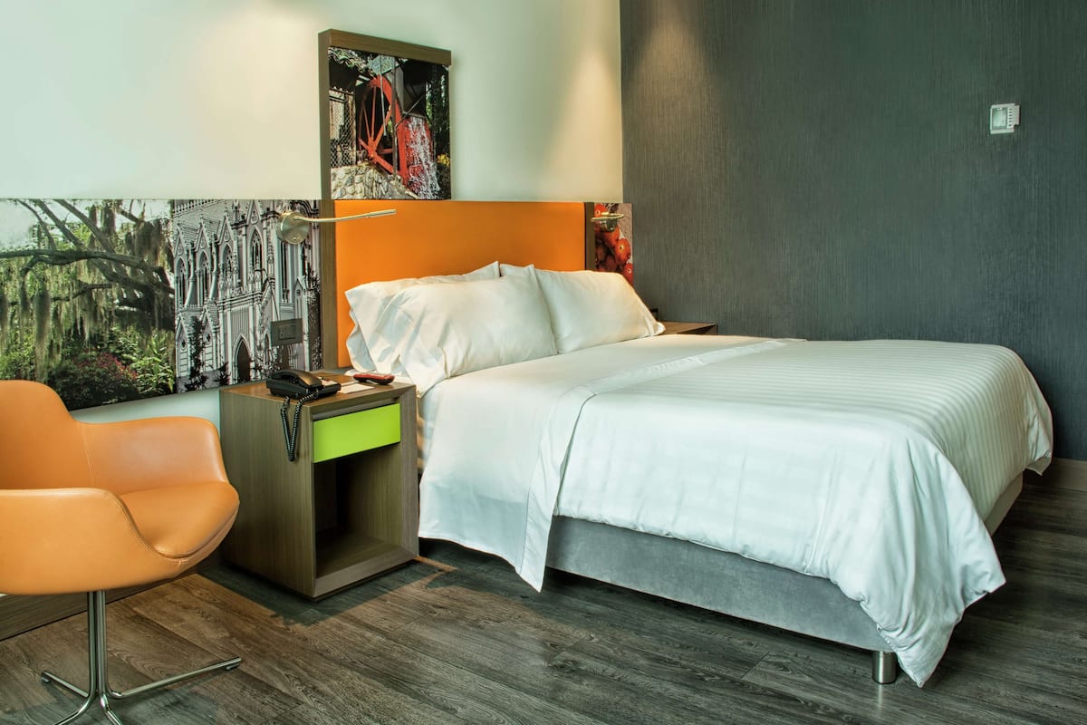 A modern hotel room with a large bed, a desk with a chair, and a painting on the wall.