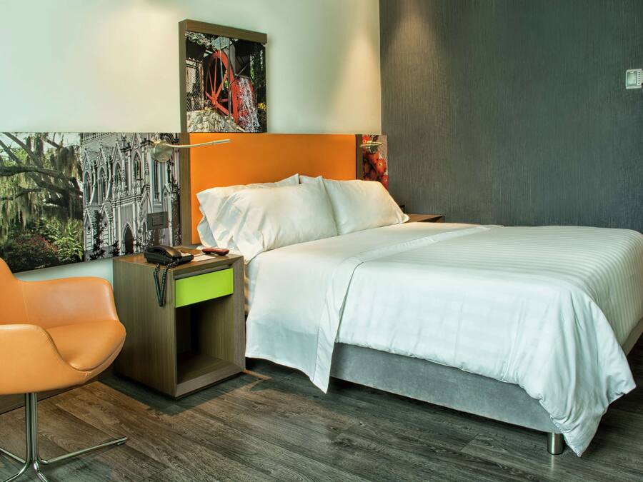 A modern hotel room with a large bed, a desk with a chair, and a painting on the wall.