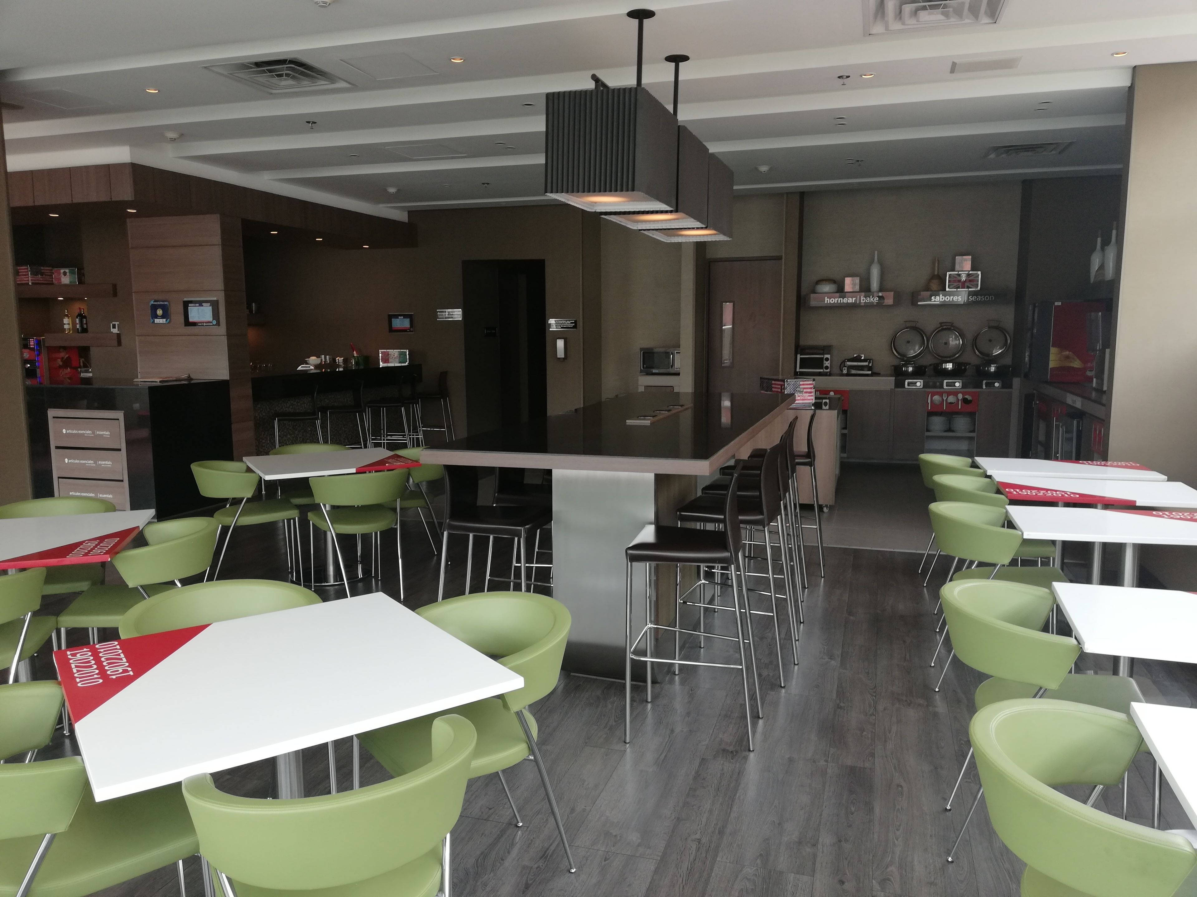 Un restaurante moderno con sillas verdes y mesas blancas, una zona de bar y una cocina al fondo.