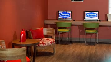 A hotel lobby with two HP computers on a desk, a red bottle, and a wooden chair with a red cushion.