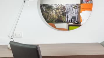 Een modern bureau met een lederen stoel, een bureaulamp en een bijzondere spiegel aan de muur die een stadsgezicht weerspiegelt.