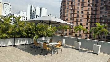 A rooftop terrace with outdoor seating, palm trees, and a view of surrounding buildings.