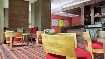 Hall d'albergo moderna con arredi in legno, cuscini rossi e un tappeto colorato a righe.