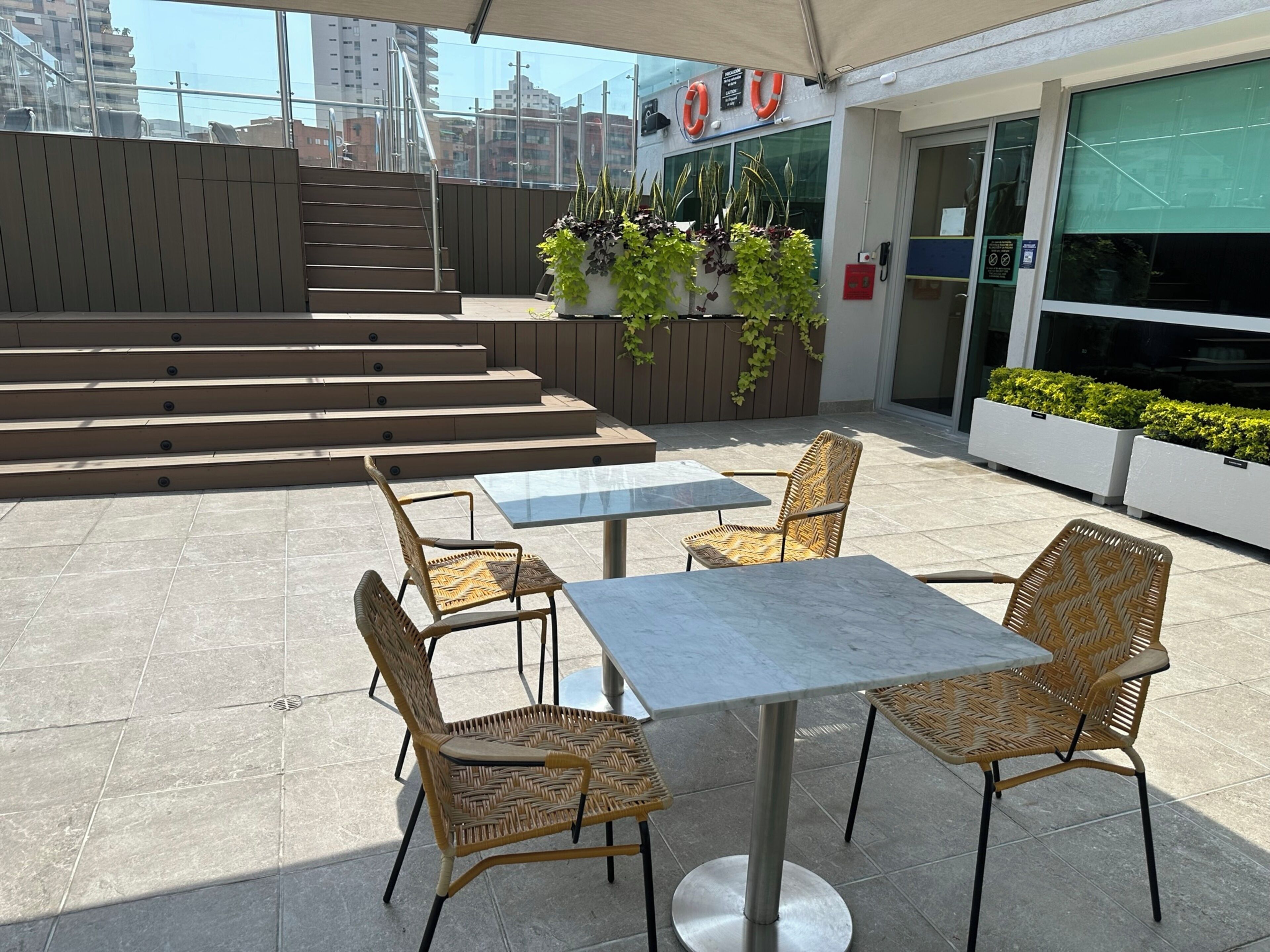 Eine Terrassengaststätte mit Korbstühlen, Marmortischen, einer Treppe und Topfpflanzen.